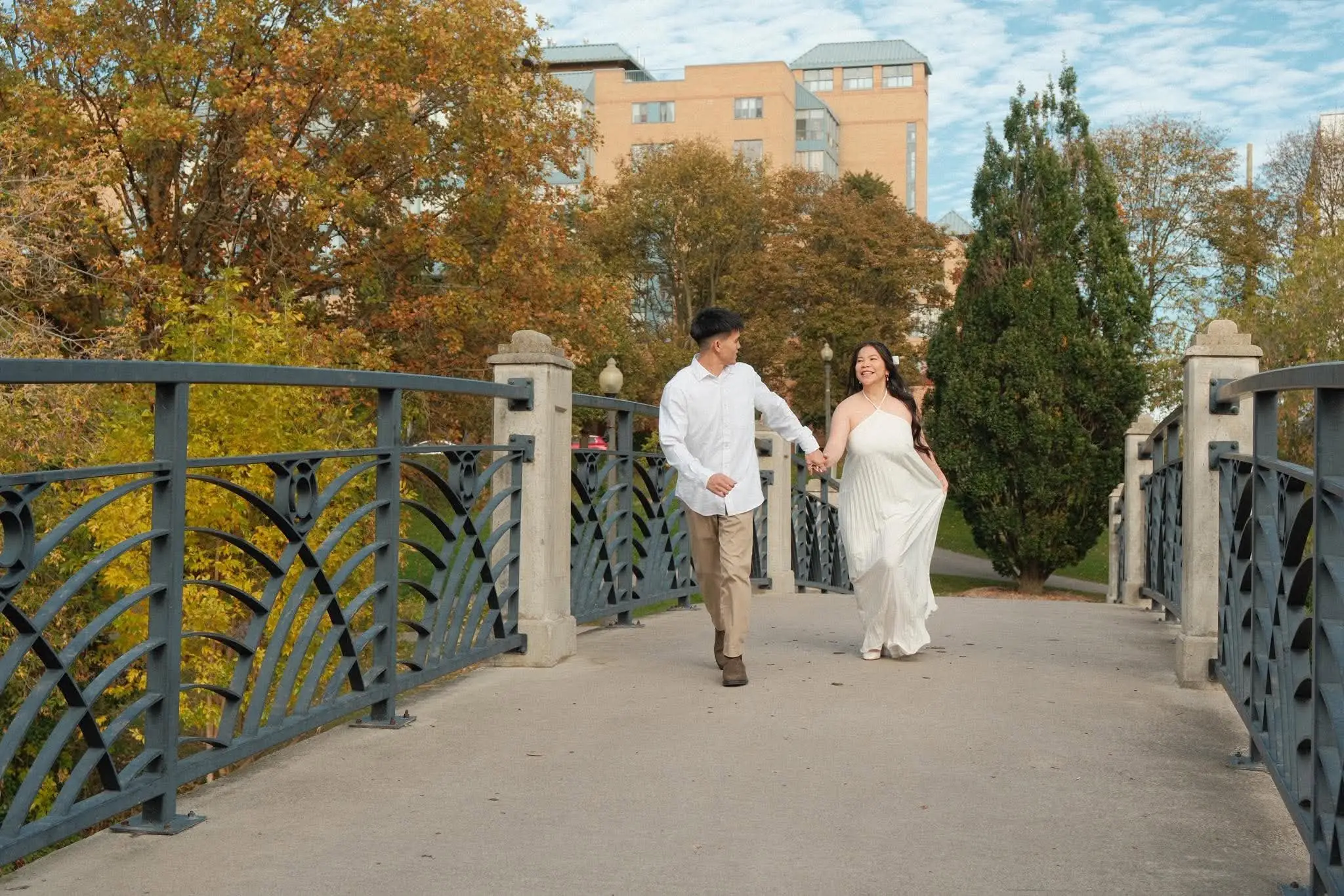 Den and Earl running hand in hand across a park bridge under a blue sky