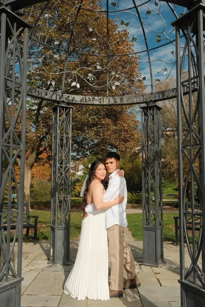 Den and Earl embracing inside an ornate iron garden gazebo