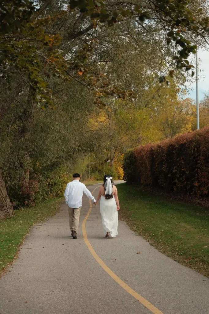 Den and Earl walking away hand in hand down a tree-lined path